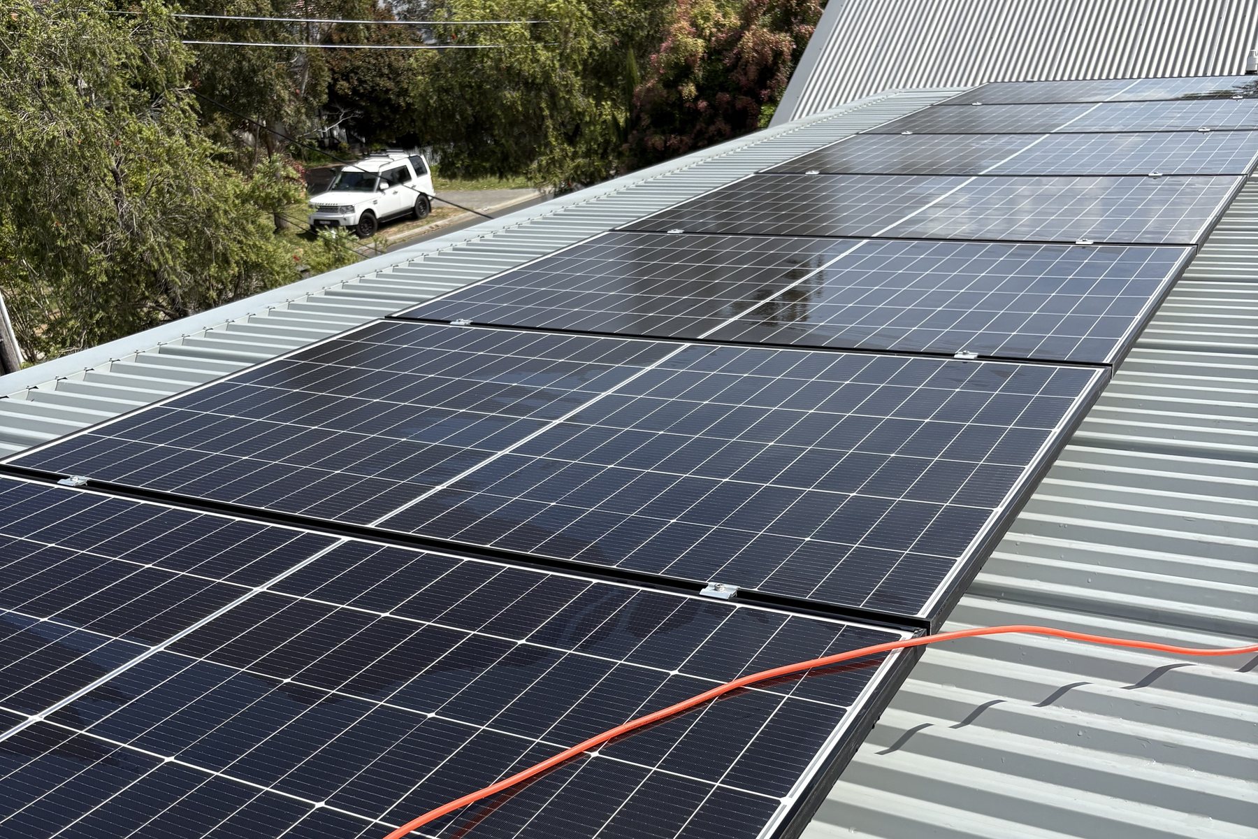 Rooftop solar panel array on a corrugated metal roof with cleaning hoses running across the panels.