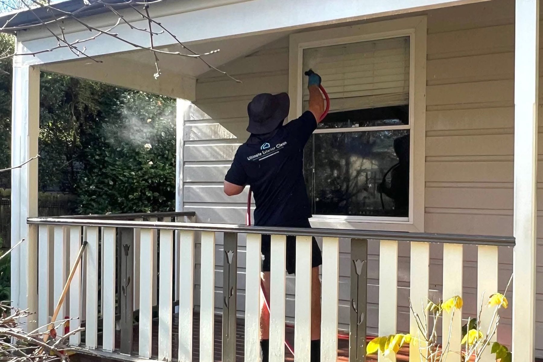 Ultimate Exterior Clean technician in branded uniform squeegeeing a verandah window on a weatherboard Sydney home.