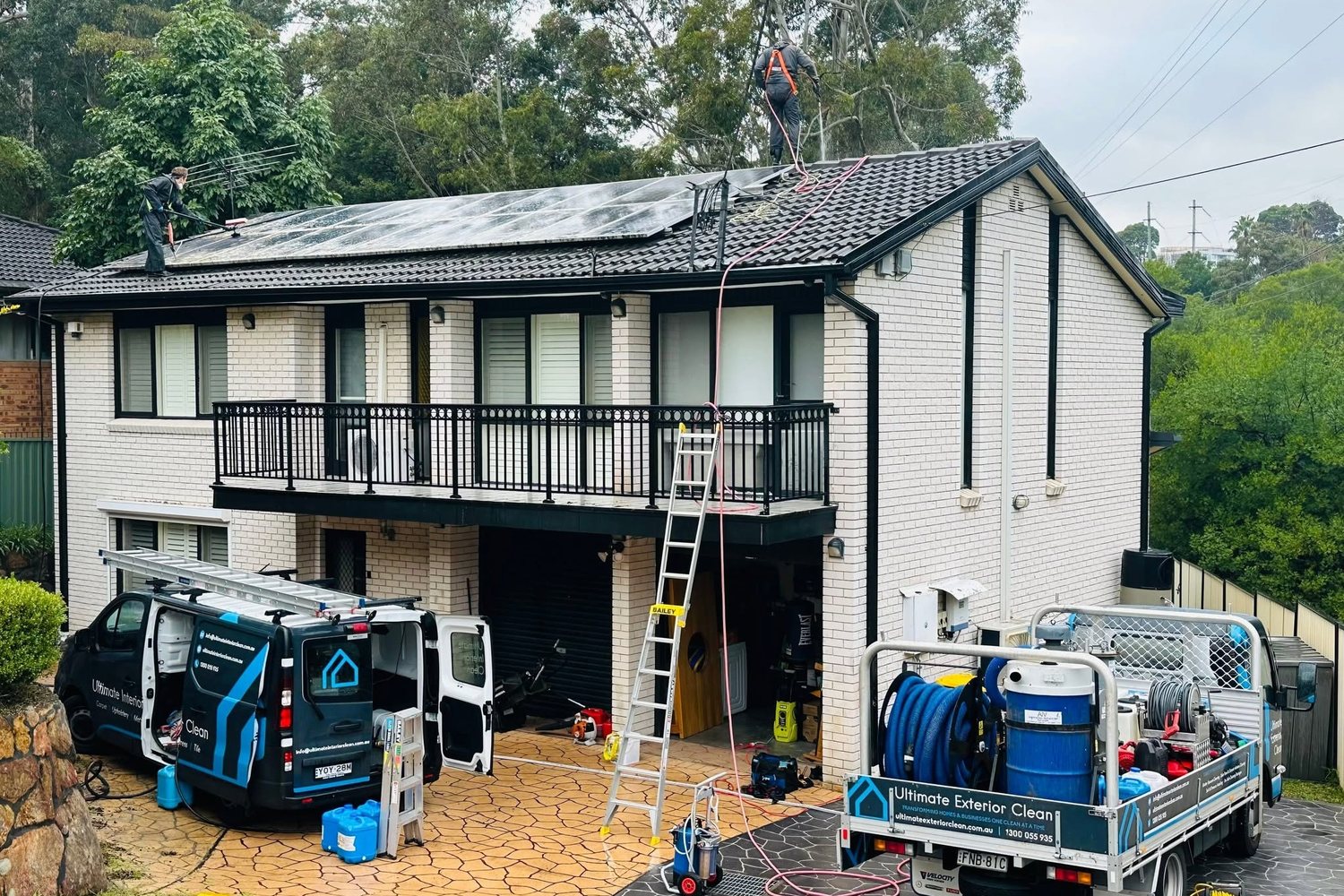 Ultimate Exterior Clean truck and van set up outside a two-storey Sydney home with roof ladder access to a solar panel array.