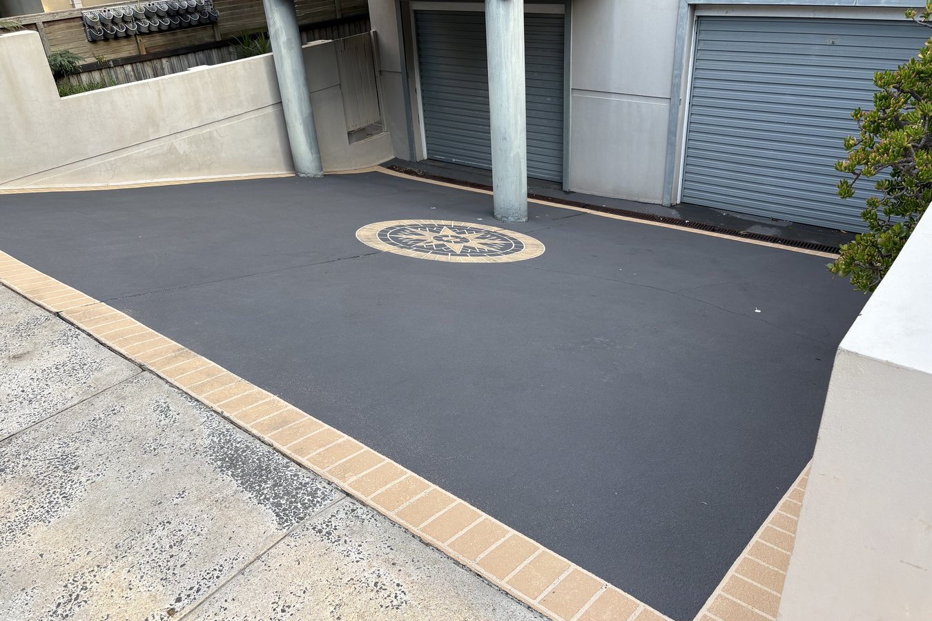 Freshly pressure-washed driveway with decorative mosaic inlay and terracotta brick edging.