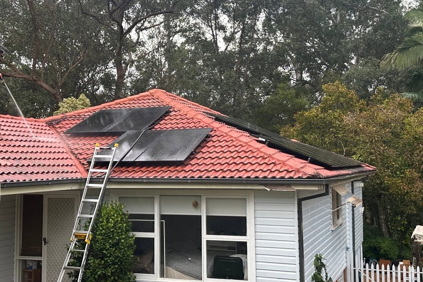 Ladder set against a terracotta tiled roof for safe access to a rooftop solar panel array.