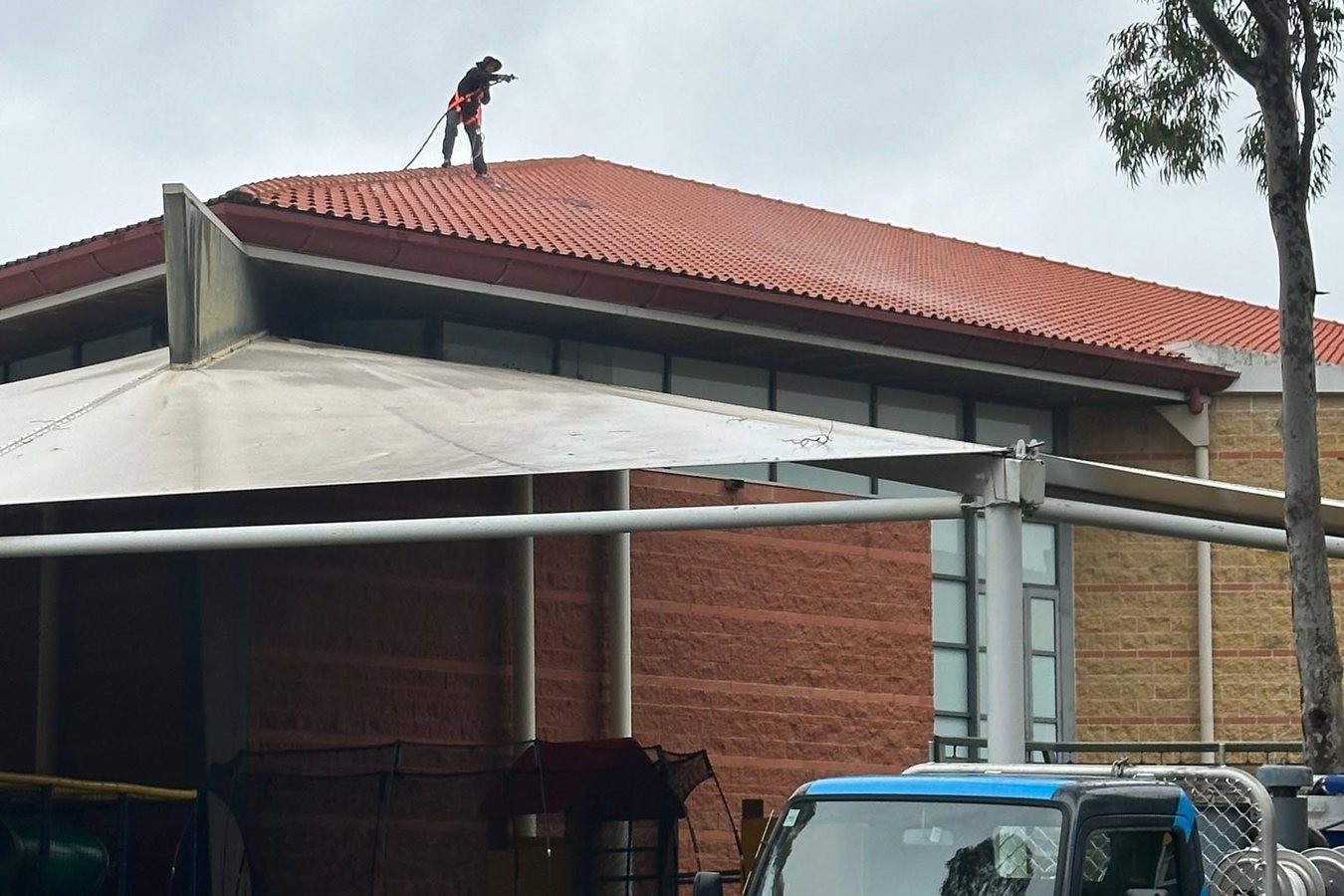 Technician working on a tiled Sydney roof with the Ultimate Exterior Clean truck parked below.