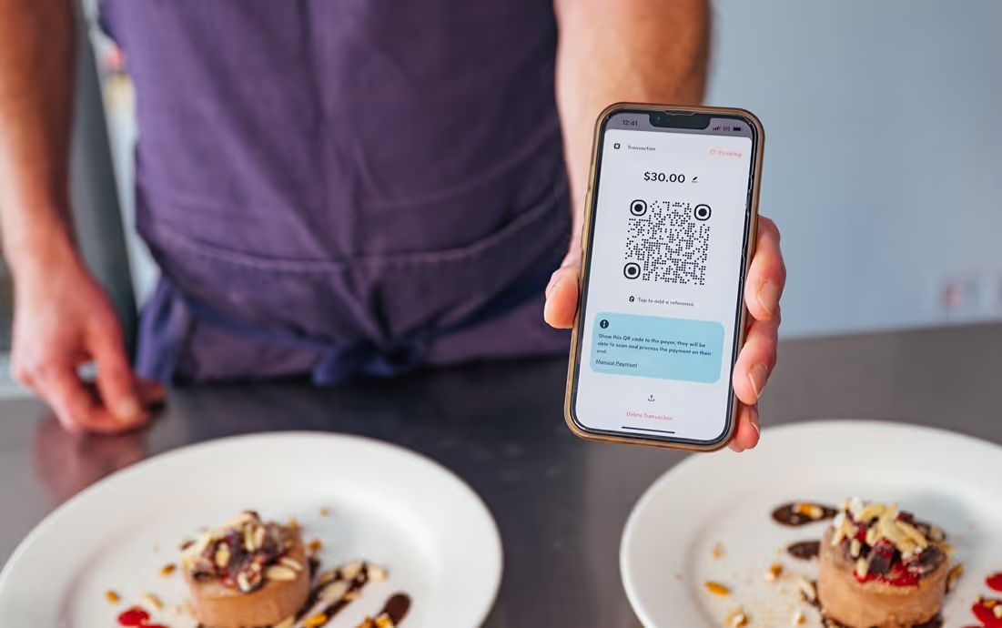 Restaurant owner presents a smartphone displaying a QR code payment screen, with gourmet dishes in the background, highlighting modern payment solutions in the culinary industry.