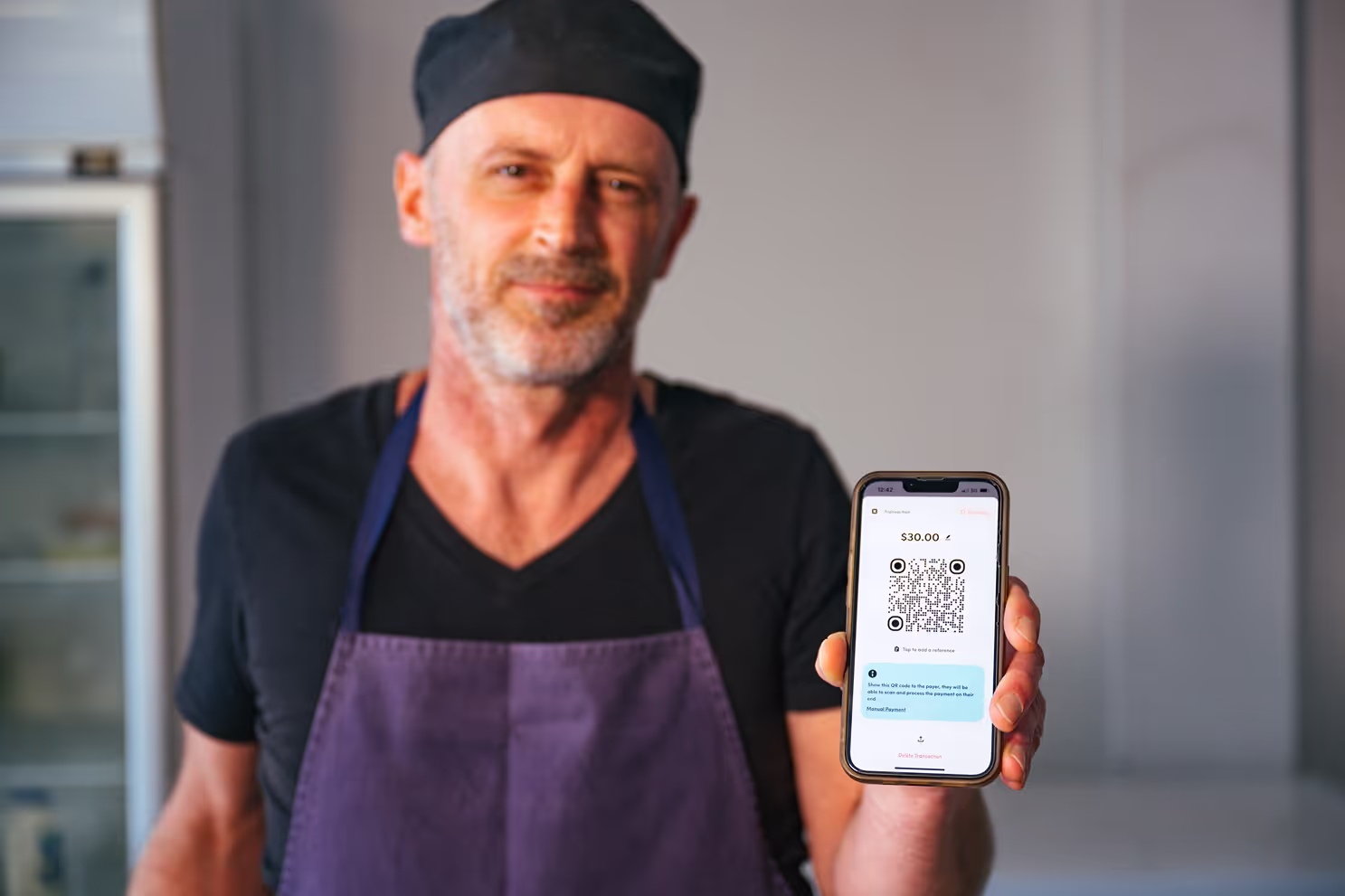 Chef in a kitchen apron proudly presenting a QR code for payment on a smartphone, signifying modern culinary business transactions.