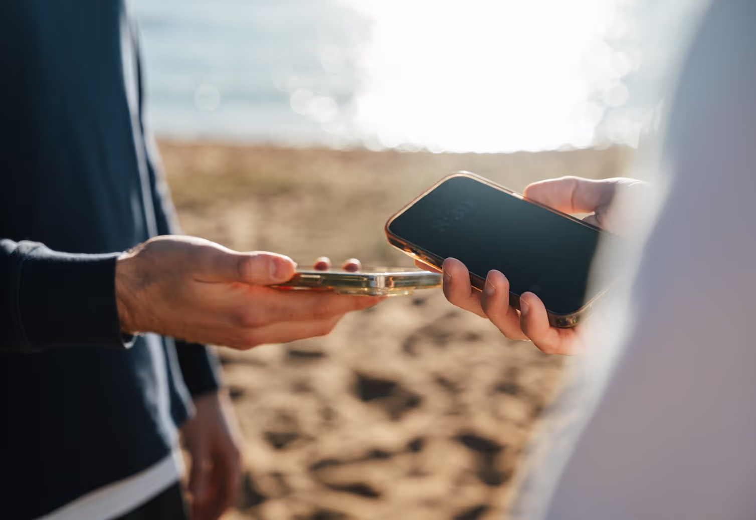 Two people holding their mobile phones close to each other on a beach, demonstrating the ease and convenience of NFC mobile payments.