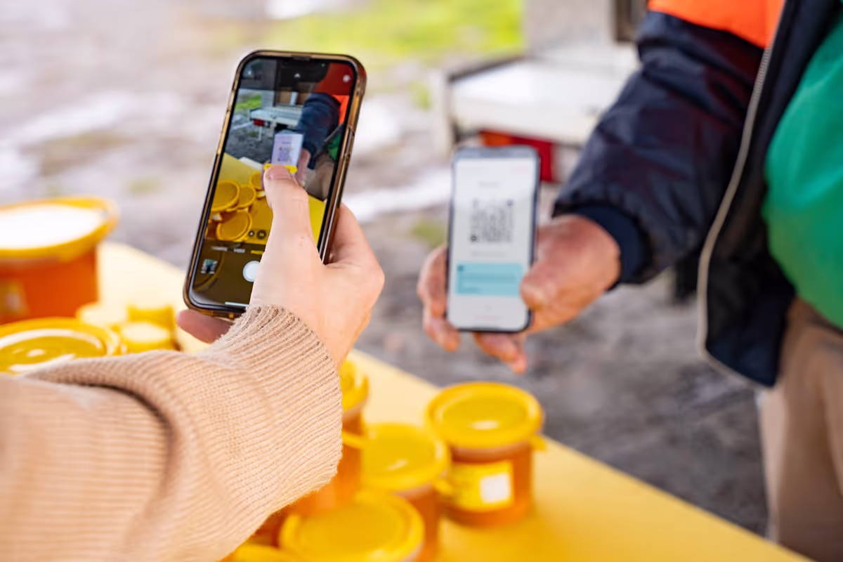 A person's hand holding a smartphone scanning a QR code from a market stall phone, showcasing a contactless payment process.