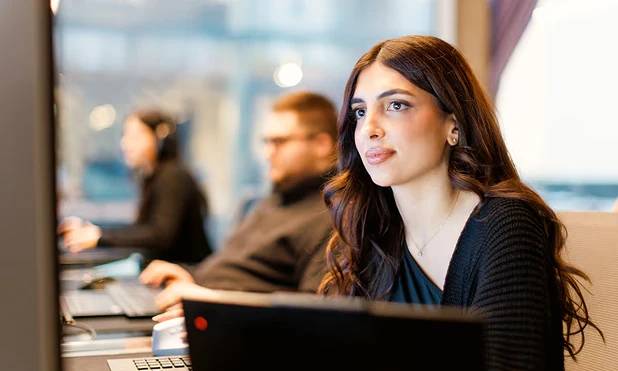 Woman concentrates on computer screen, two other people work at the desk in the office.