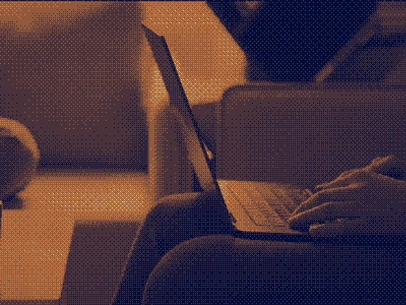 Person sits on sofa and works on a laptop in the evening with warm light in the room.