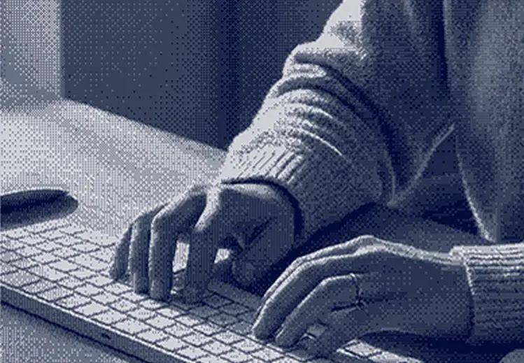 Person types on a white computer keyboard, wears a knitted sweater and a ring on his right hand.