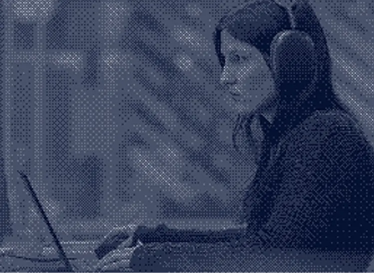 Woman with long dark hair wears headphones and works on a laptop in a room with sound-absorbing walls.