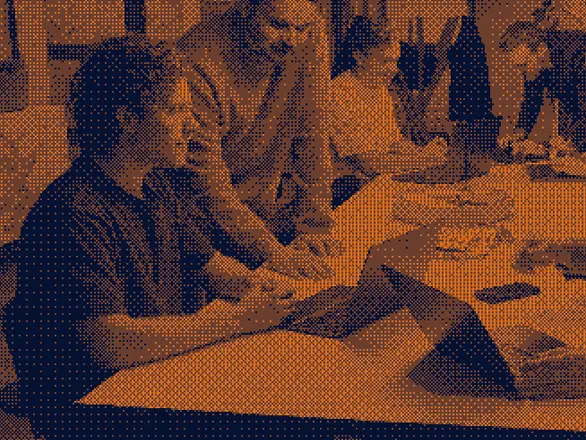 A group of people sitting around a table and working together, some using laptops and notepads.