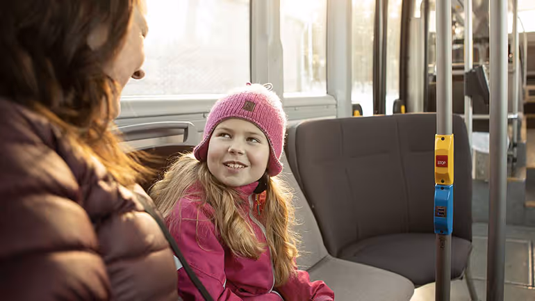 Närbild på mamma och dotter som sitter på buss och tittar på varandra.