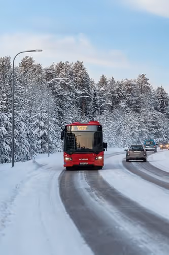 Linje 9 trafikerar snötäckta gator med träd i vinterskrud bakom.