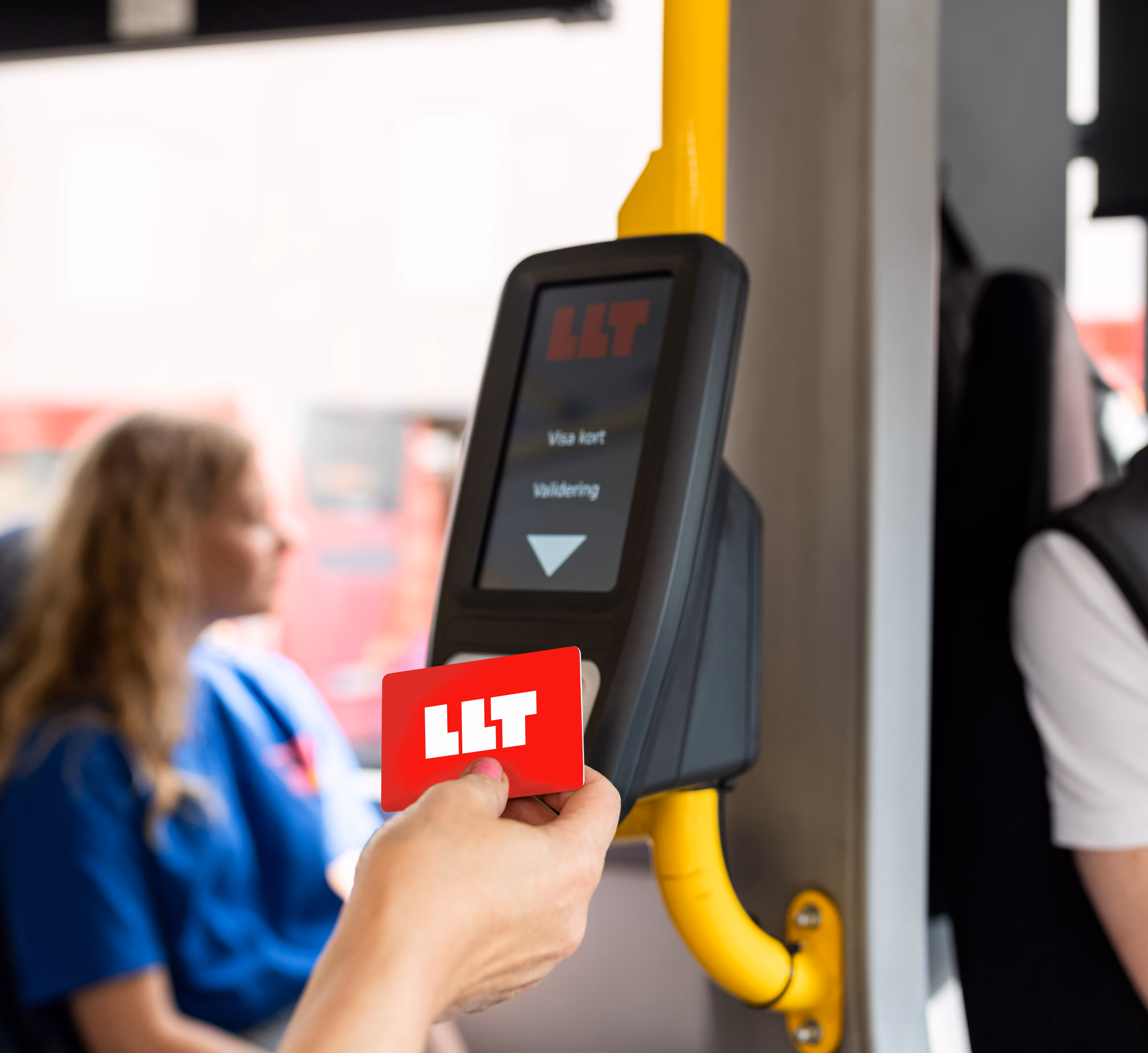 Hand håller ett rött LLT-busskort framför en biljettautomat på en buss.