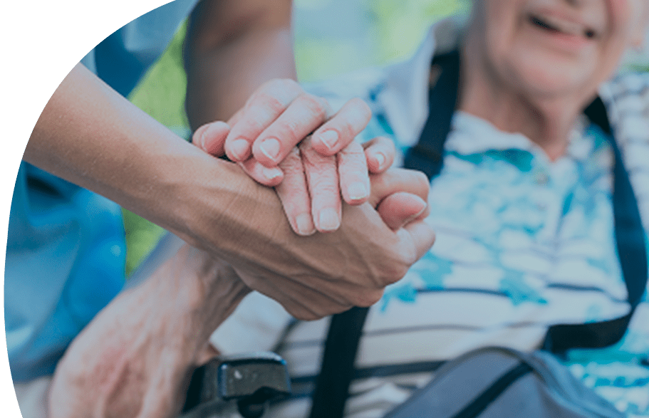 Eine Pflegekraft hält liebevoll die Hand einer älteren Person im Rollstuhl – eine symbolische Geste für Vertrauen, Unterstützung und menschliche Nähe in der Altenpflege.