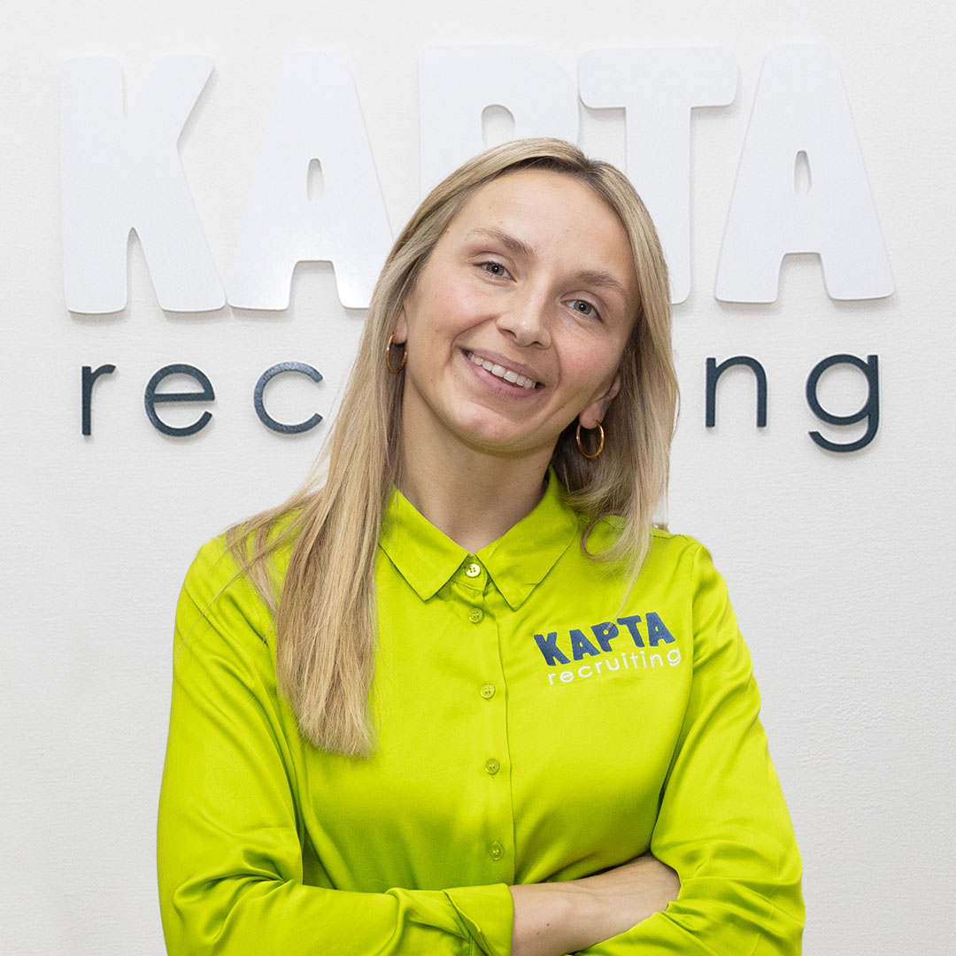 Marie von KAPTA Recruiting steht freundlich lächelnd vor dem Firmenlogo – Expertin für internationale Fachkräftegewinnung mit Herz und Kompetenz.