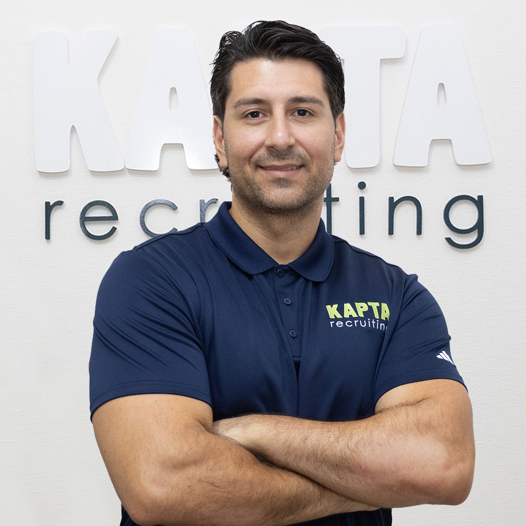 Ignacio von KAPTA Recruiting steht selbstbewusst vor dem Firmenlogo, mit verschränkten Armen und einem freundlichen Lächeln – Experte für internationale Pflegekräfte.