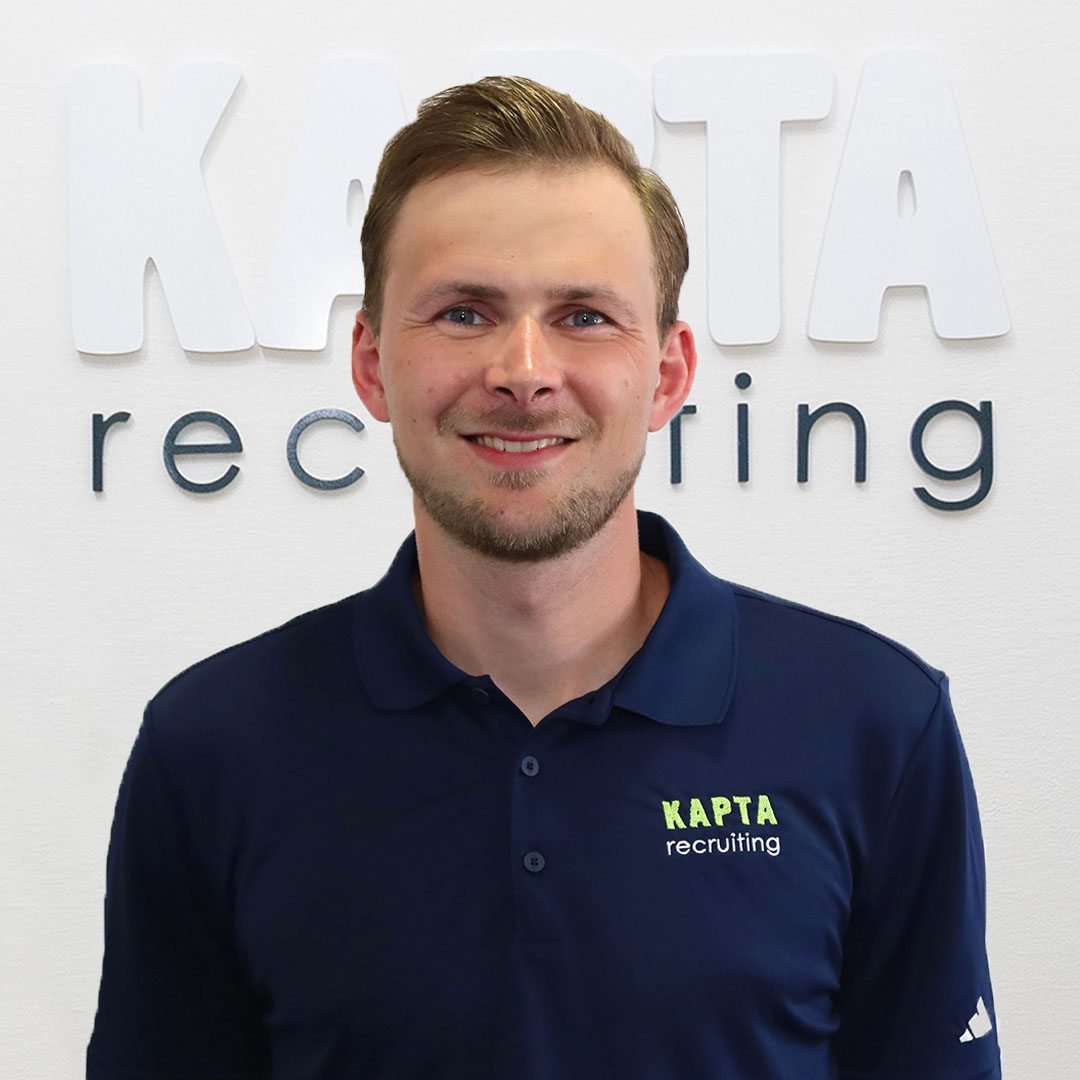 Ignacio von KAPTA Recruiting steht selbstbewusst vor dem Firmenlogo, mit verschränkten Armen und einem freundlichen Lächeln – Experte für internationale Pflegekräfte.