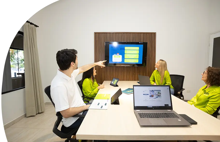 Ein Team von KAPTA Recruiting sitzt in einem modernen Besprechungsraum und verfolgt eine Präsentation auf einem Bildschirm. Ein Mitarbeiter zeigt auf die Präsentationsfolie, während andere aufmerksam zuhören – Symbol für Teamarbeit, Strategie und Vision.