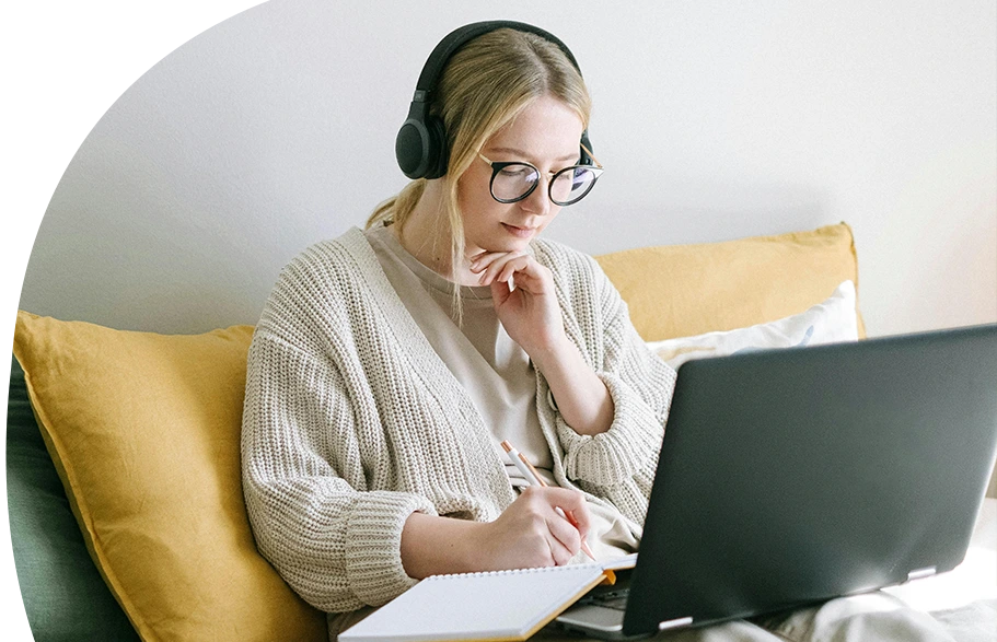 Eine Frau mit langen blonden Haaren und auffällig grünem Hemd steht mit dem Rücken zur Kamera und hält vor einer Gruppe junger Erwachsener einen Vortrag. Die Teilnehmenden sitzen in einem hellen Raum mit großen Fenstern, tragen weiße T-Shirts und wirken aufmerksam und interessiert.