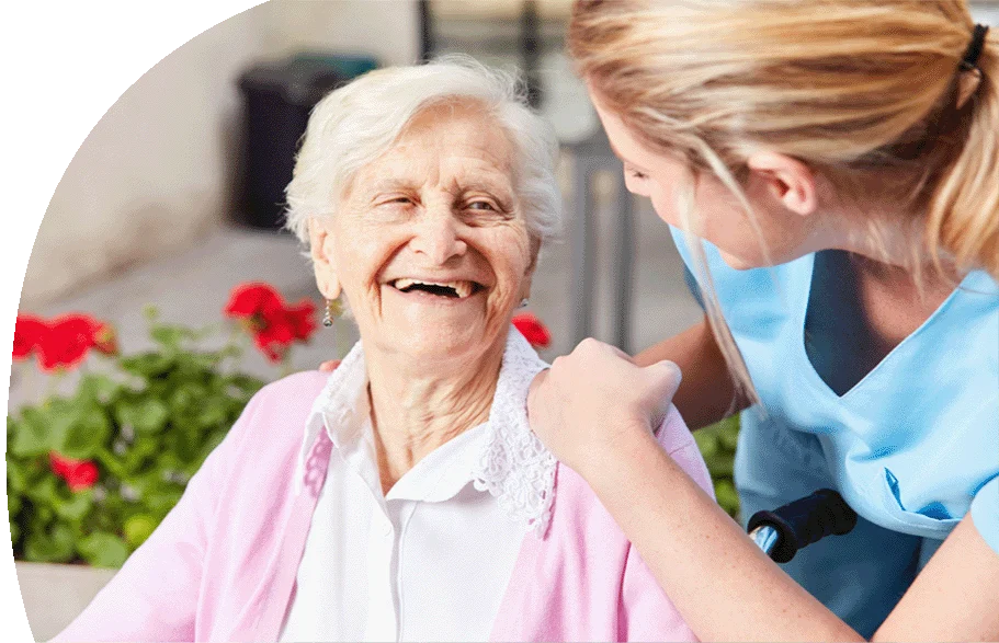 Eine Frau mit langen blonden Haaren und auffällig grünem Hemd steht mit dem Rücken zur Kamera und hält vor einer Gruppe junger Erwachsener einen Vortrag. Die Teilnehmenden sitzen in einem hellen Raum mit großen Fenstern, tragen weiße T-Shirts und wirken aufmerksam und interessiert.