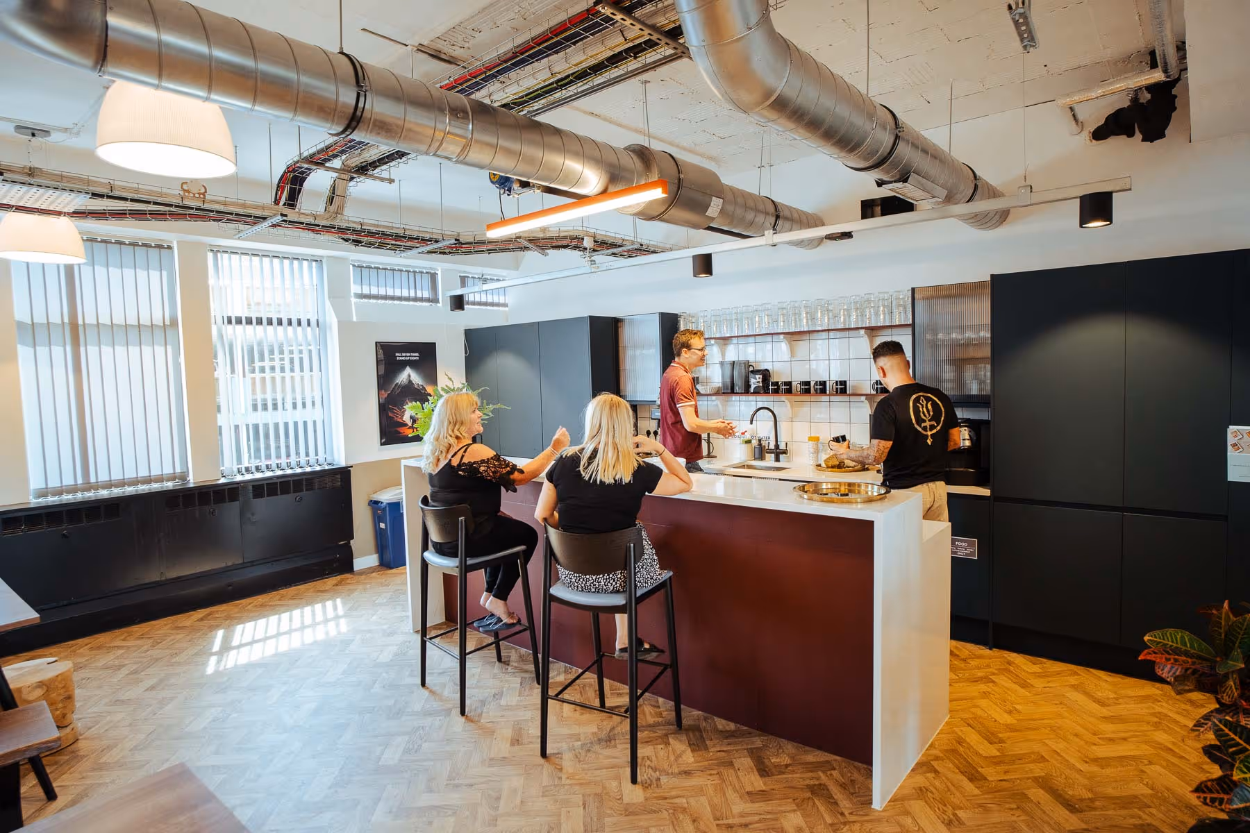 A group of people sat around an island in a kitchen area