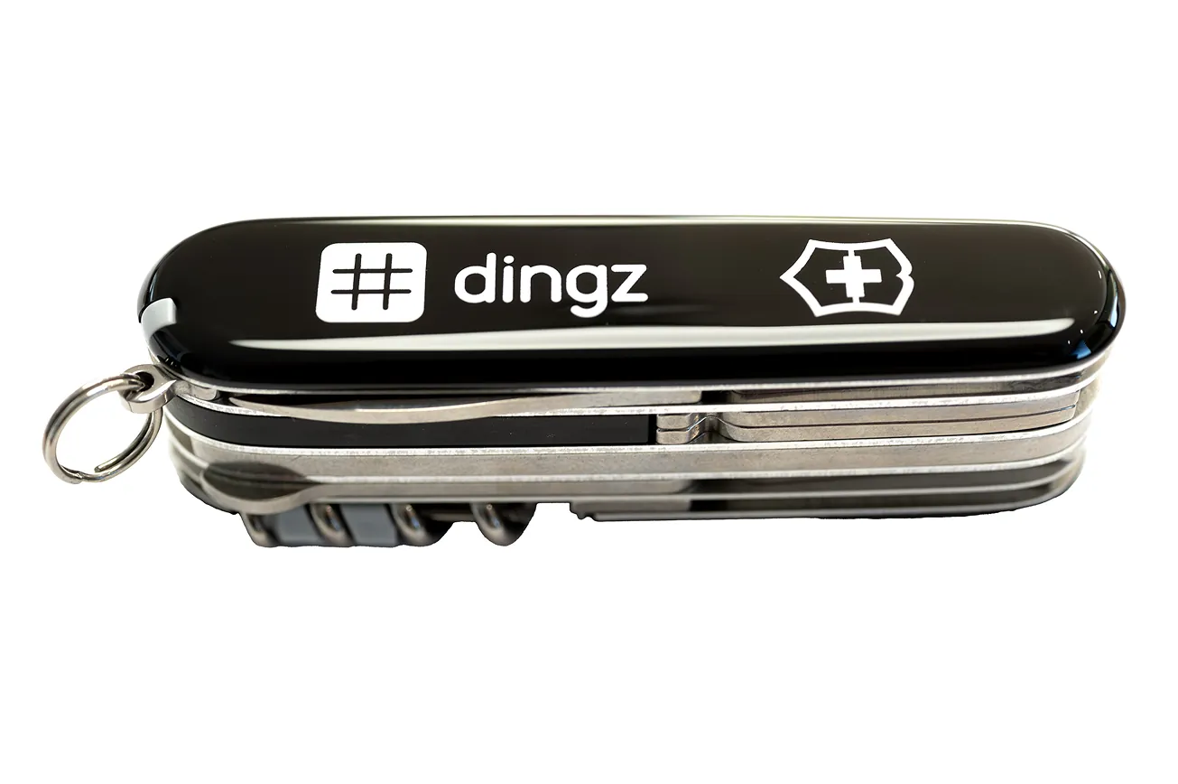 Black Swiss Army-style multi-tool pocket knife featuring the text '# dingz' and a white cross logo on the handle with multiple folded tools visible on the side.