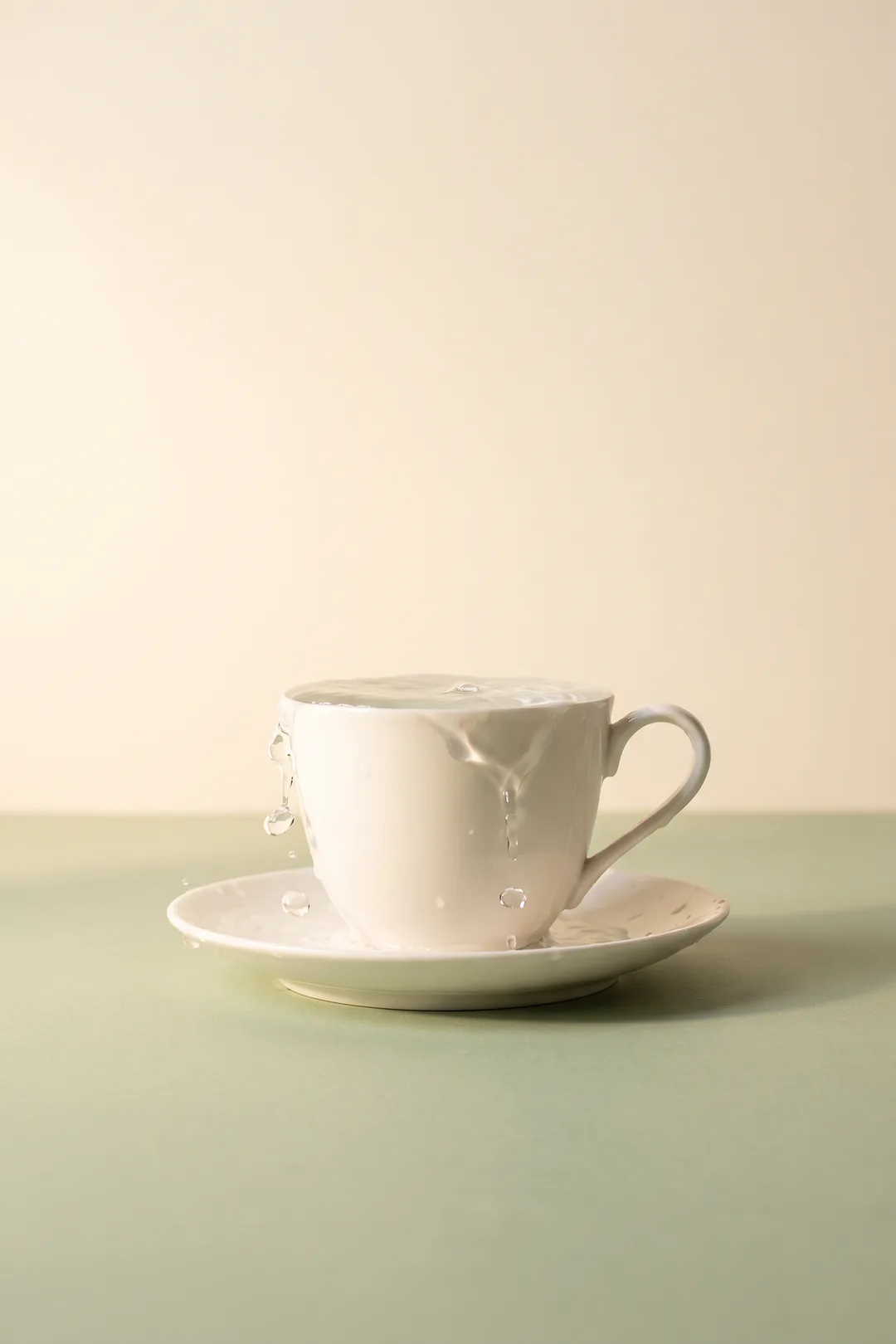 Imagen ilustrativa: taza de porcelana blanca que rebosa de agua sobre un plato, con gotas suspendidas en el aire