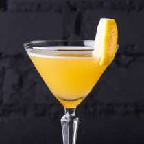 Kieliszek koktajlu z jasnopomarańczowym drinkiem i plasterkiem cytryny na krawędzi.