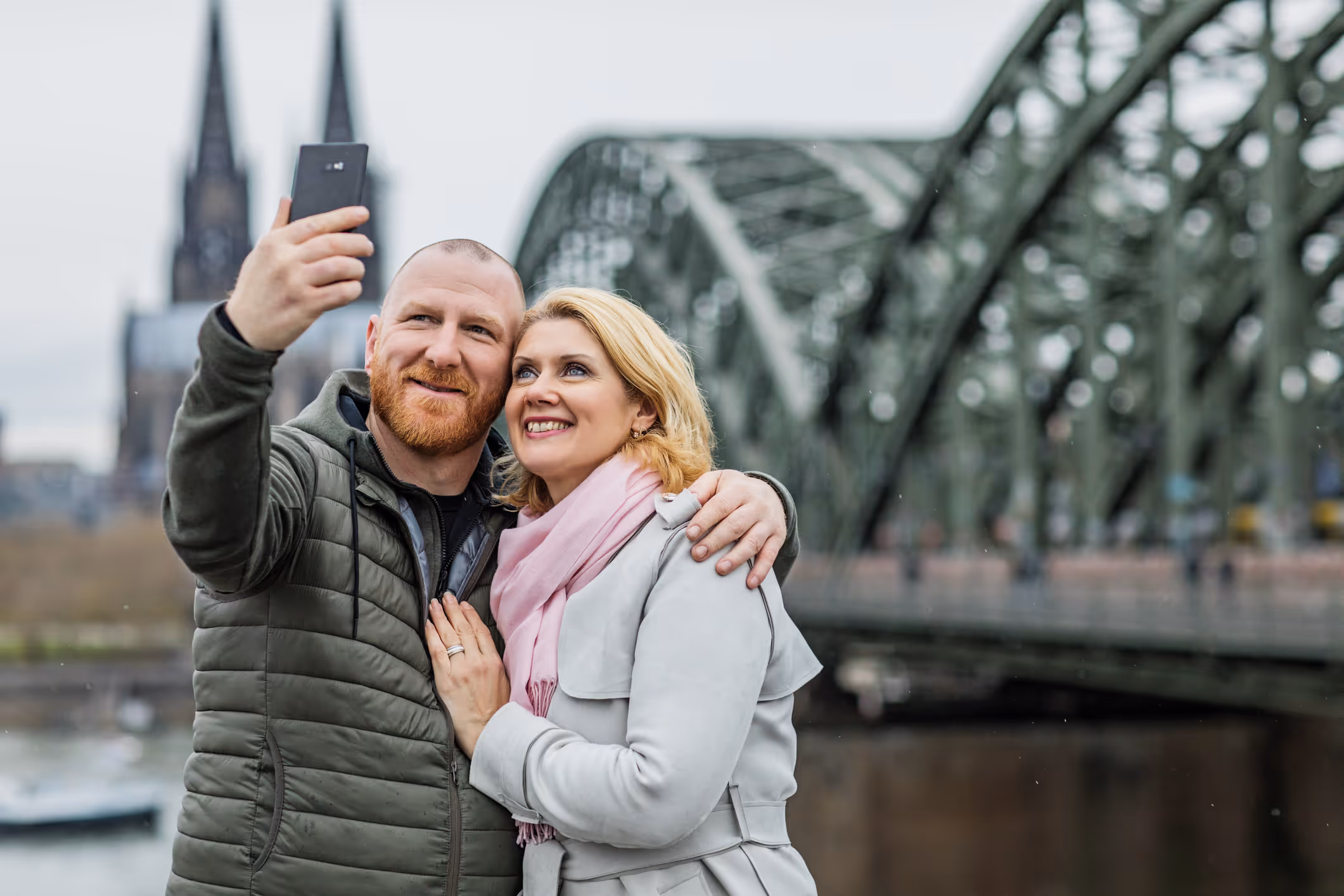 Paar macht Selfie mit Smartphone vor der Hohenzollernbrücke und Dom in Köln