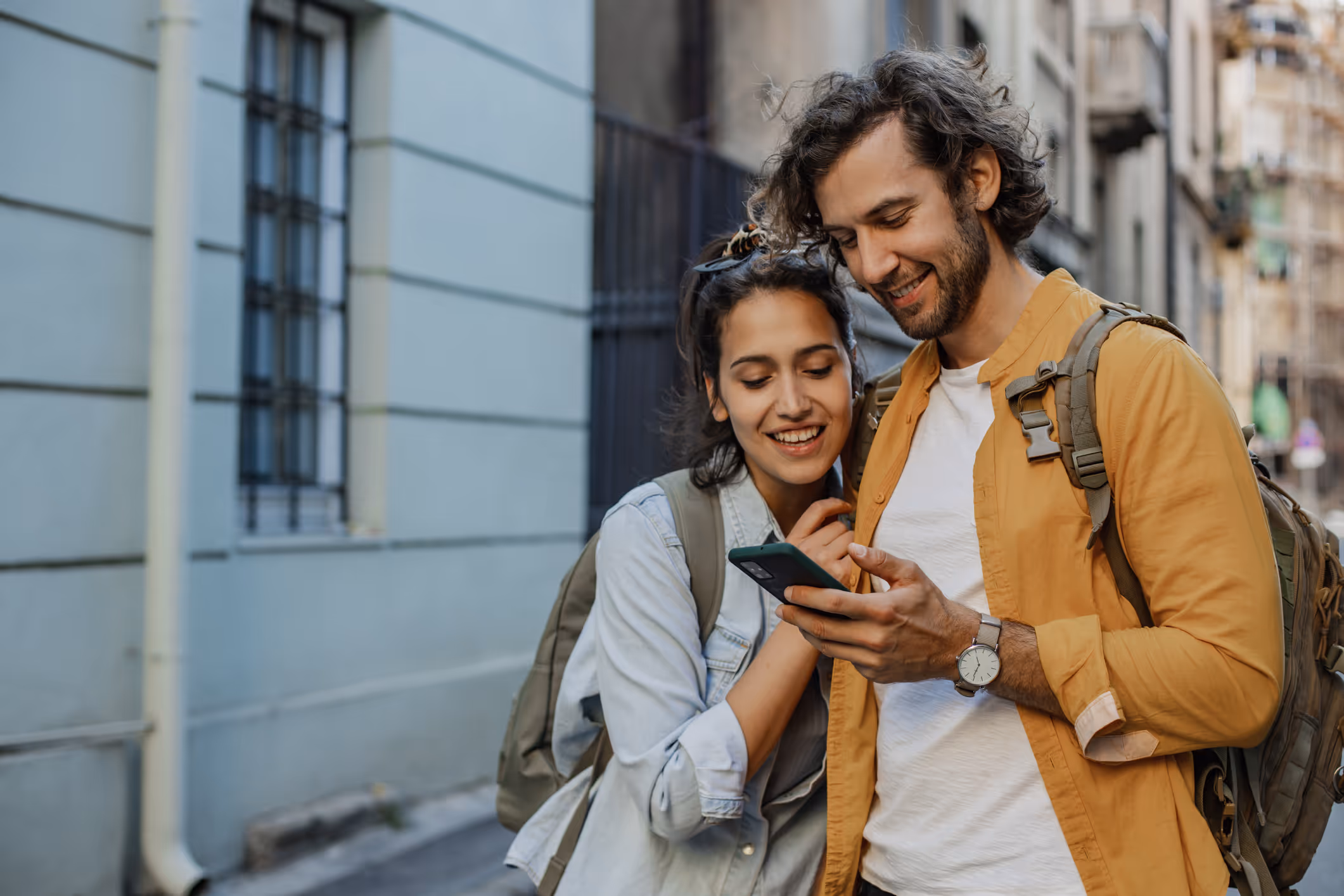 Ein Paar steht auf der Straße und schaut lächelnd gemeinsam auf ein Smartphone