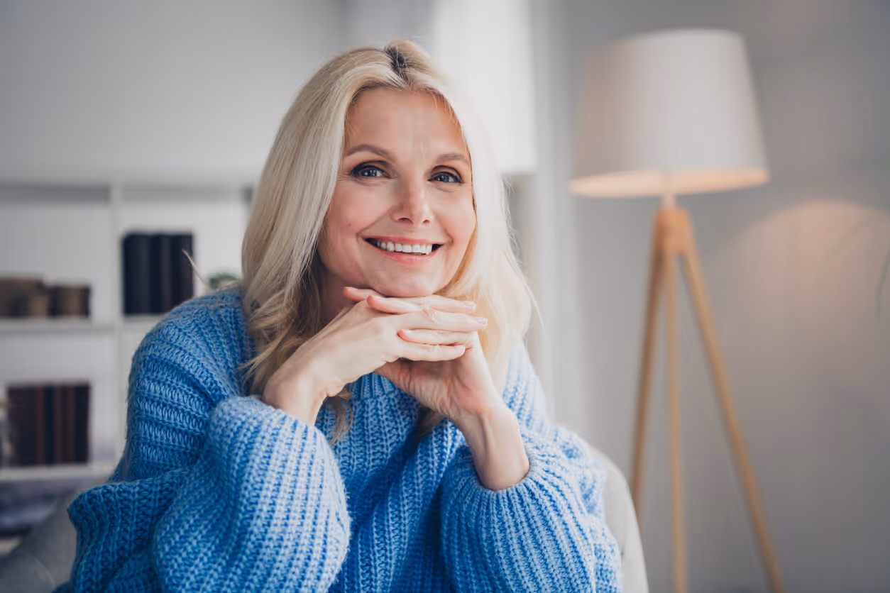 Eine lächelnde Frau mit blonden Haaren stützt ihr Kinn auf ihre Hände