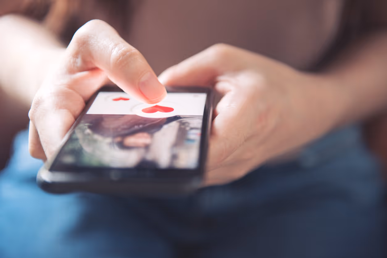 Eine Hand tippt auf ein Smartphone, auf dem ein Herz-Symbol angezeigt wird
