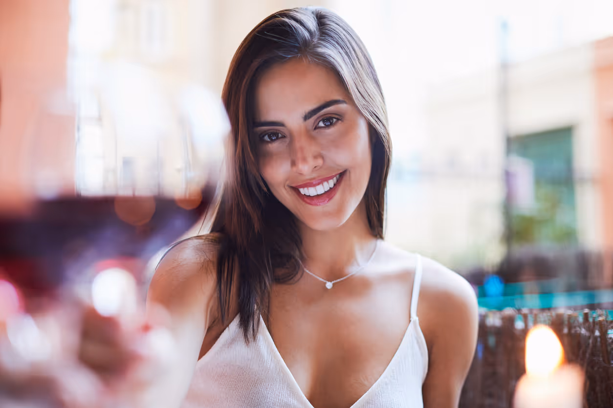 Eine Frau lächelt in die Kamera und stößt dabei mit einem Glas Wein an