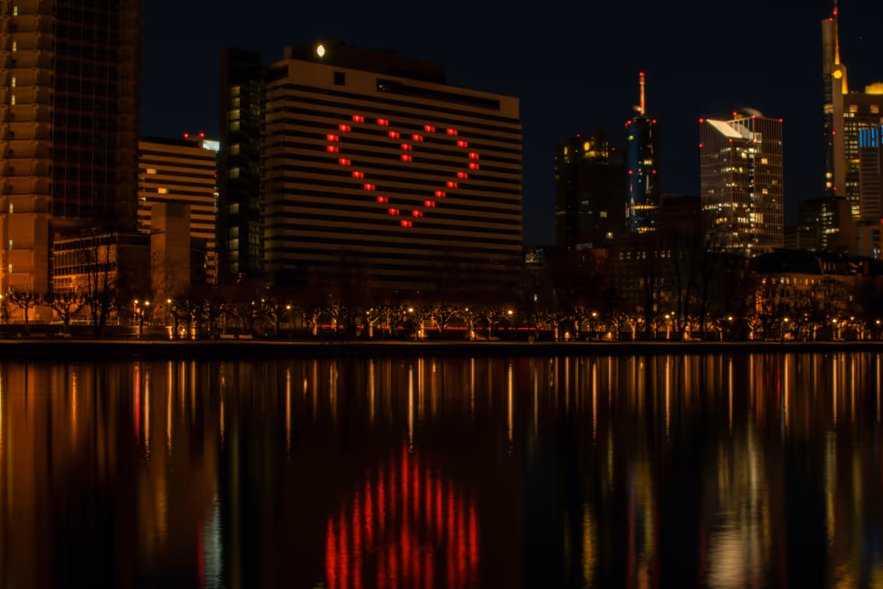 Nachtsicht von Frankfurt am Main mit einem Gebäude, das ein Herz aus roten Lichtern zeigt, reflektiert im Wasser
