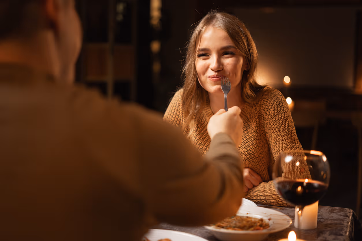 Mann, der seine Frau mit Gabel füttert beim romantischem Abendessen im Restaurant