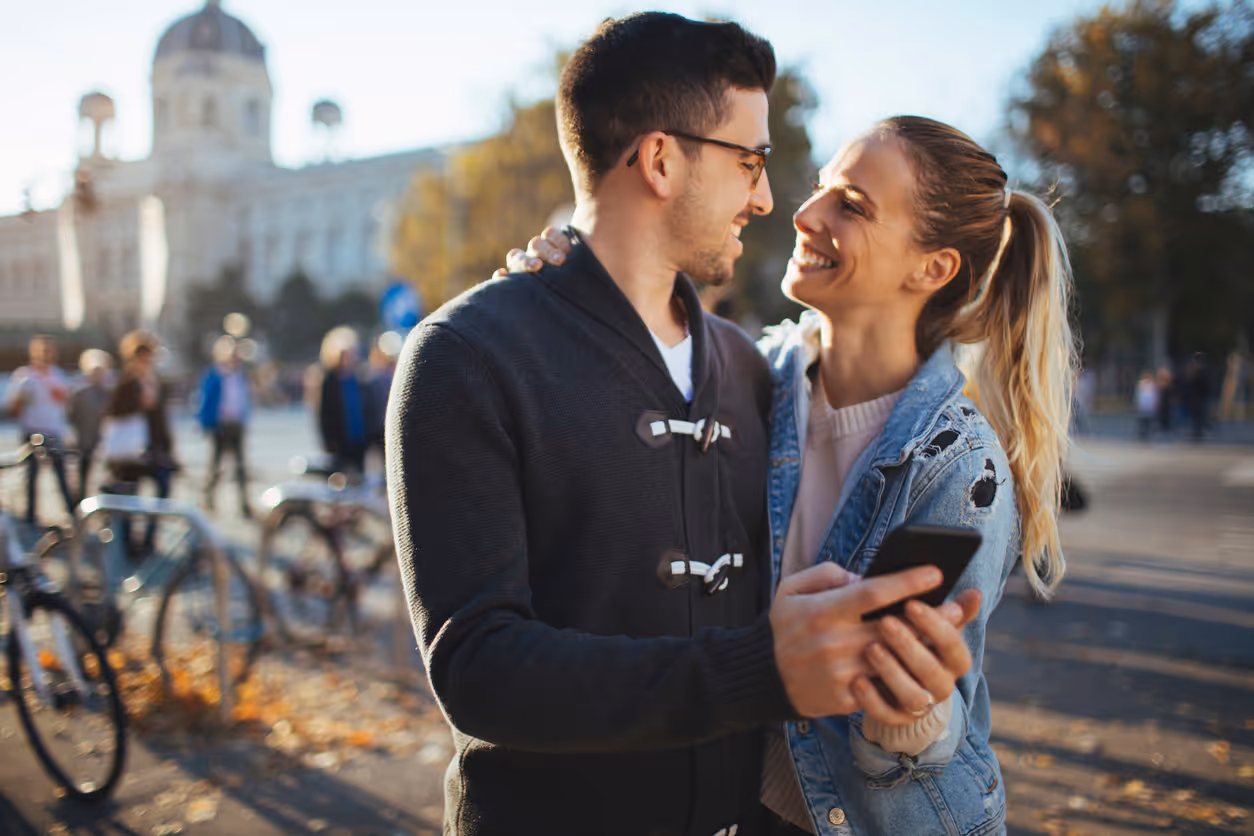 Glückliches Paar genießt sonnigen Herbsttag draußen in der Stadt und ist am Handy