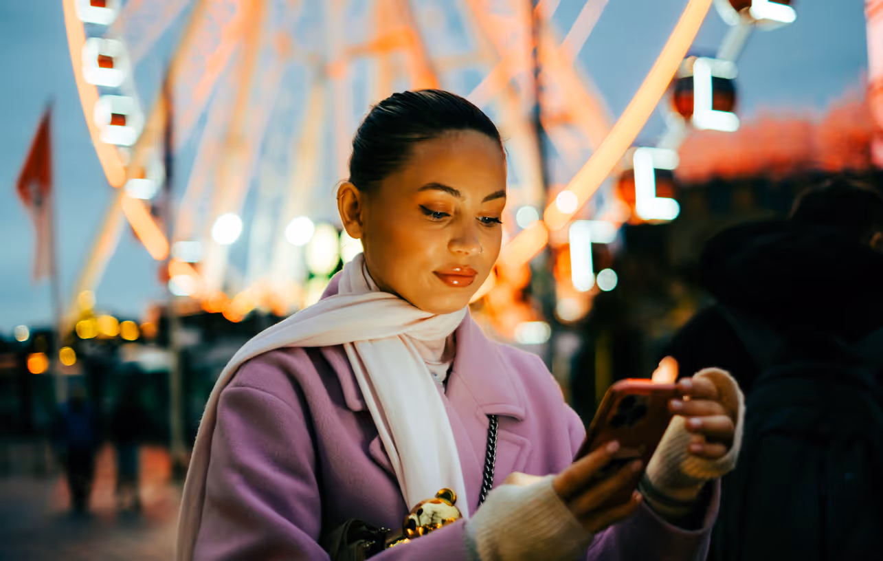 Frau, die am Abend auf der Rheinkirmes ein Mobiltelefon benutzt