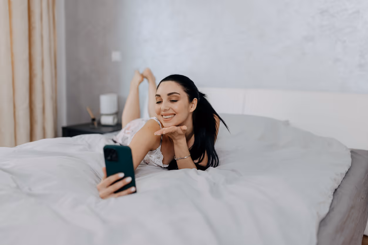  Eine Frau liegt auf dem Bett und sendet einen Handkuss über ihr Smartphone