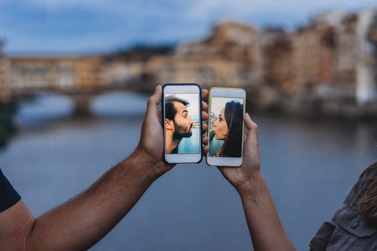 Ein Paar hält zwei Smartphones, auf denen jeweils ein Foto von ihnen zu sehen ist. Das Paar blickt sich durch die Smartphones gegenseitig an