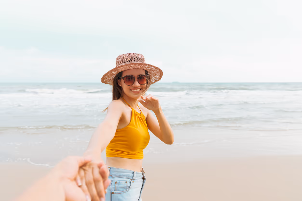 Eine Frau hält die Hand einer anderen Person und lächelt glücklich am Strand
