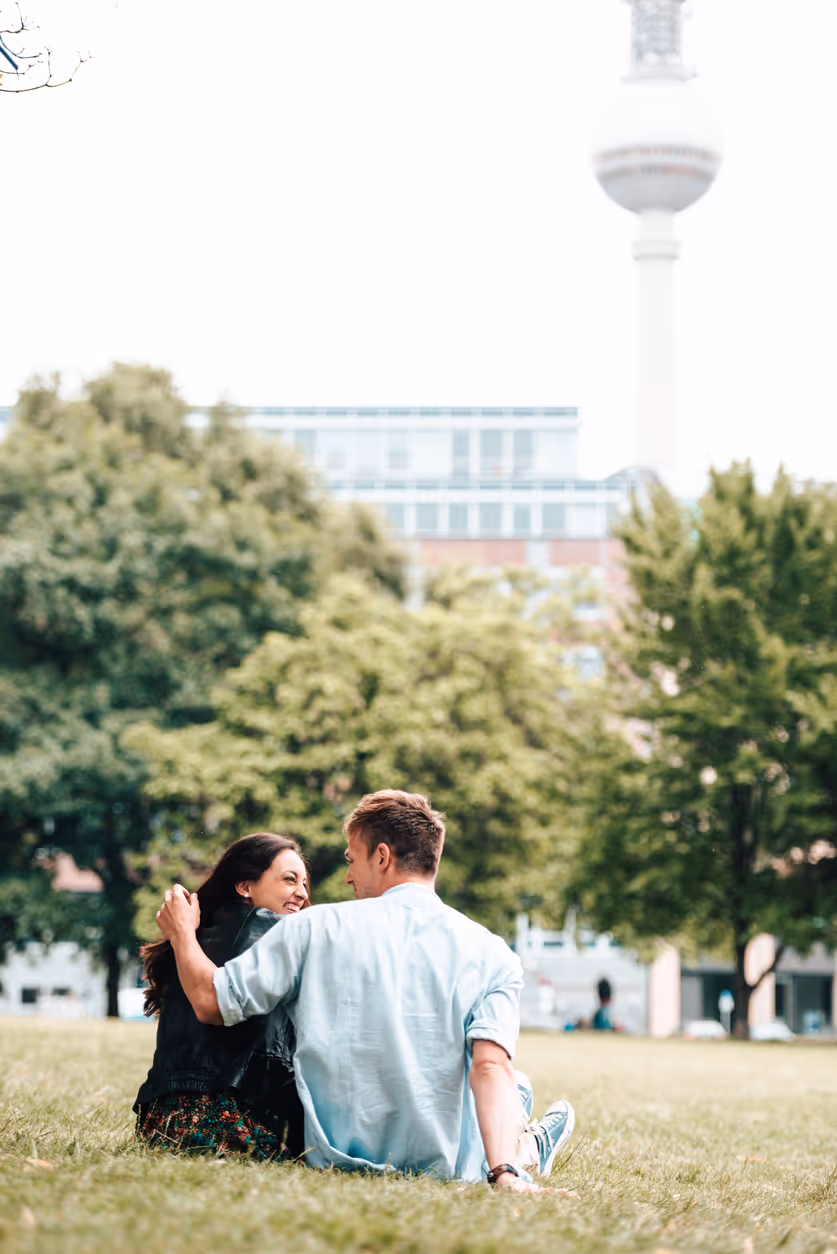 Ein Paar sitzt Arm in Arm in einem Park. Im Hintergrund ist der Fernsehturm von Berlin zu sehen