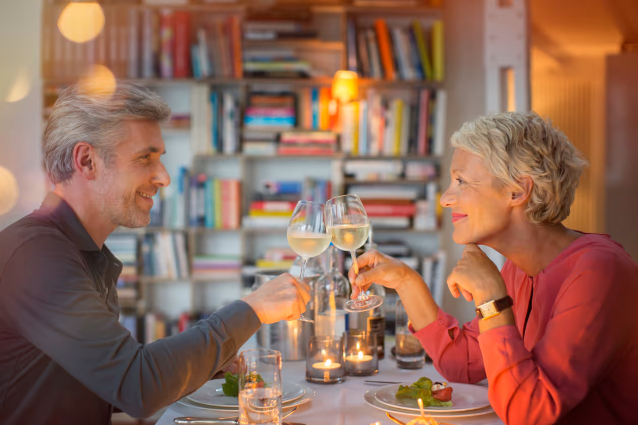 Älteres Paar stößt beim romantischen Abendessen mit Weißwein an