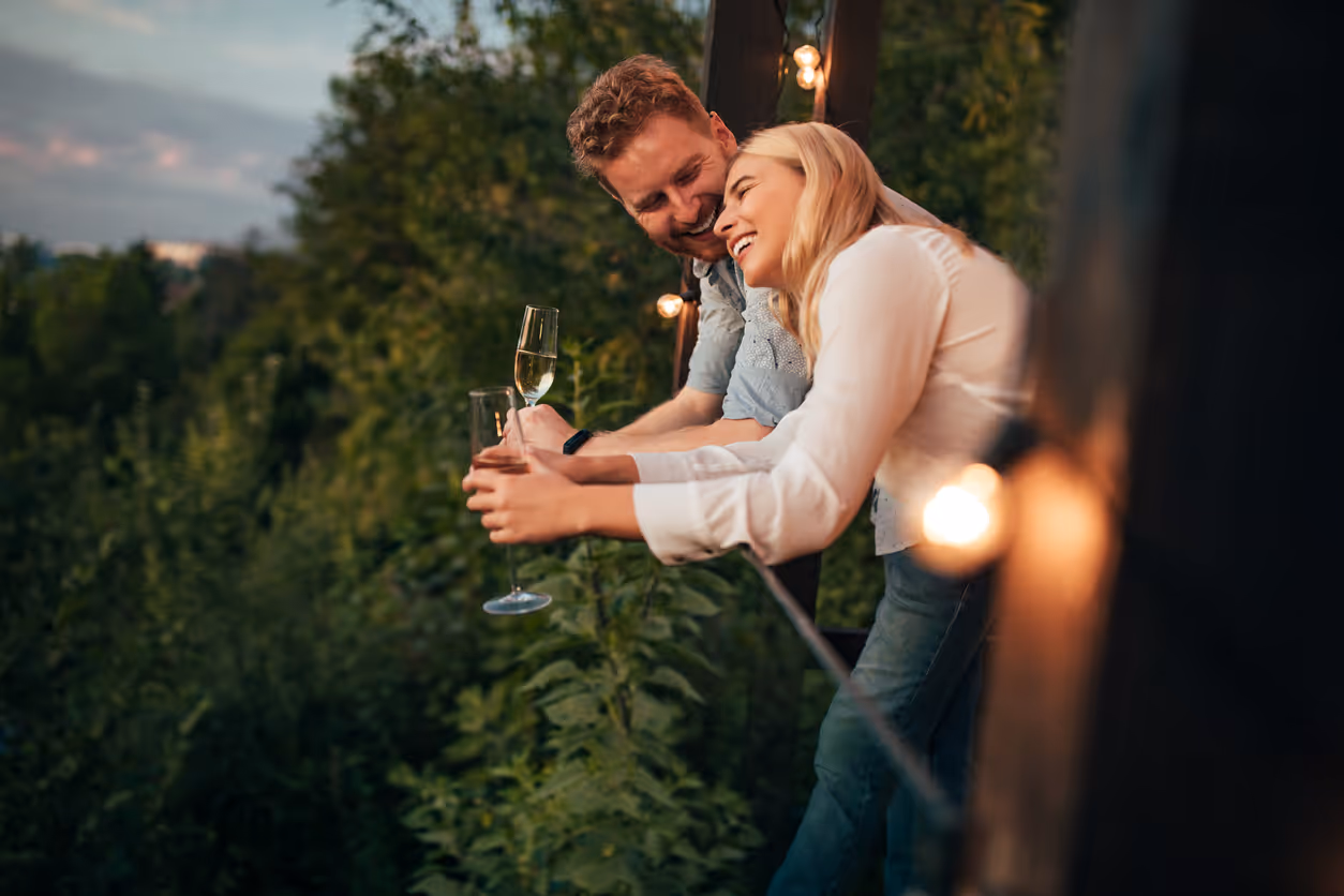 Junges Paar trinkt Sekt auf der Terrasse und genießt die Aussicht ins Grüne