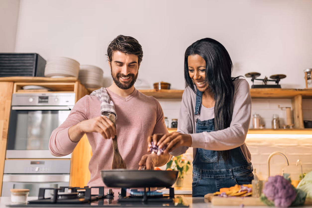 Ein Mann und eine Frau in einer Küche beim Kochen. Beide lachen