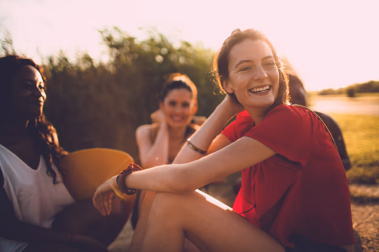 Drei Frauen, die während des Sonnenuntergangs auf einer Wiese sitzen und lächeln