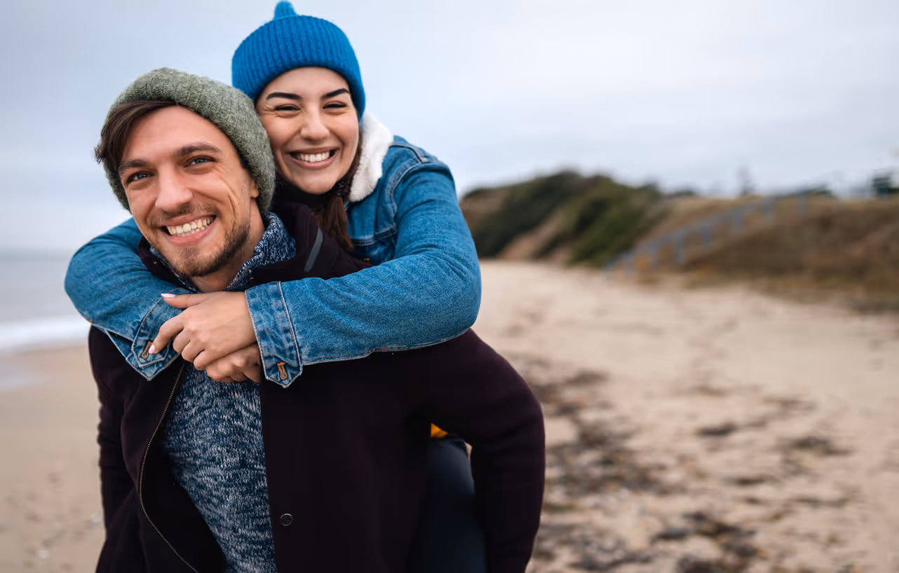 Glückliche Frau ist huckepack bei einem Mann am Strand im Winter.