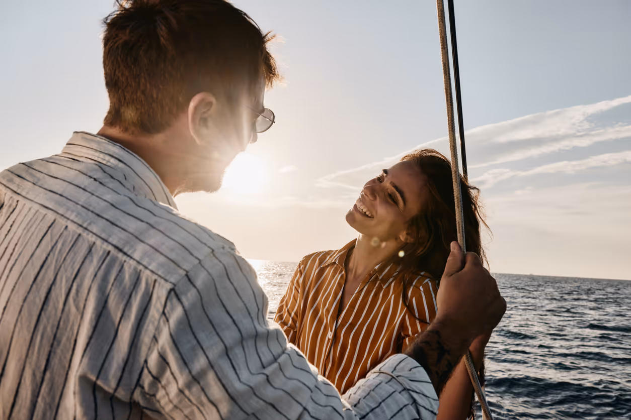 Glückliche Frau, die mit ihrem Freund auf einer Yacht bei Sonnenuntergang spricht.