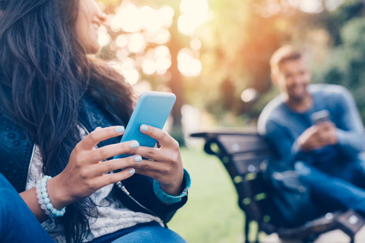 Glückliches Paar mit Smartphones im Stadtpark auf zwei Bänken