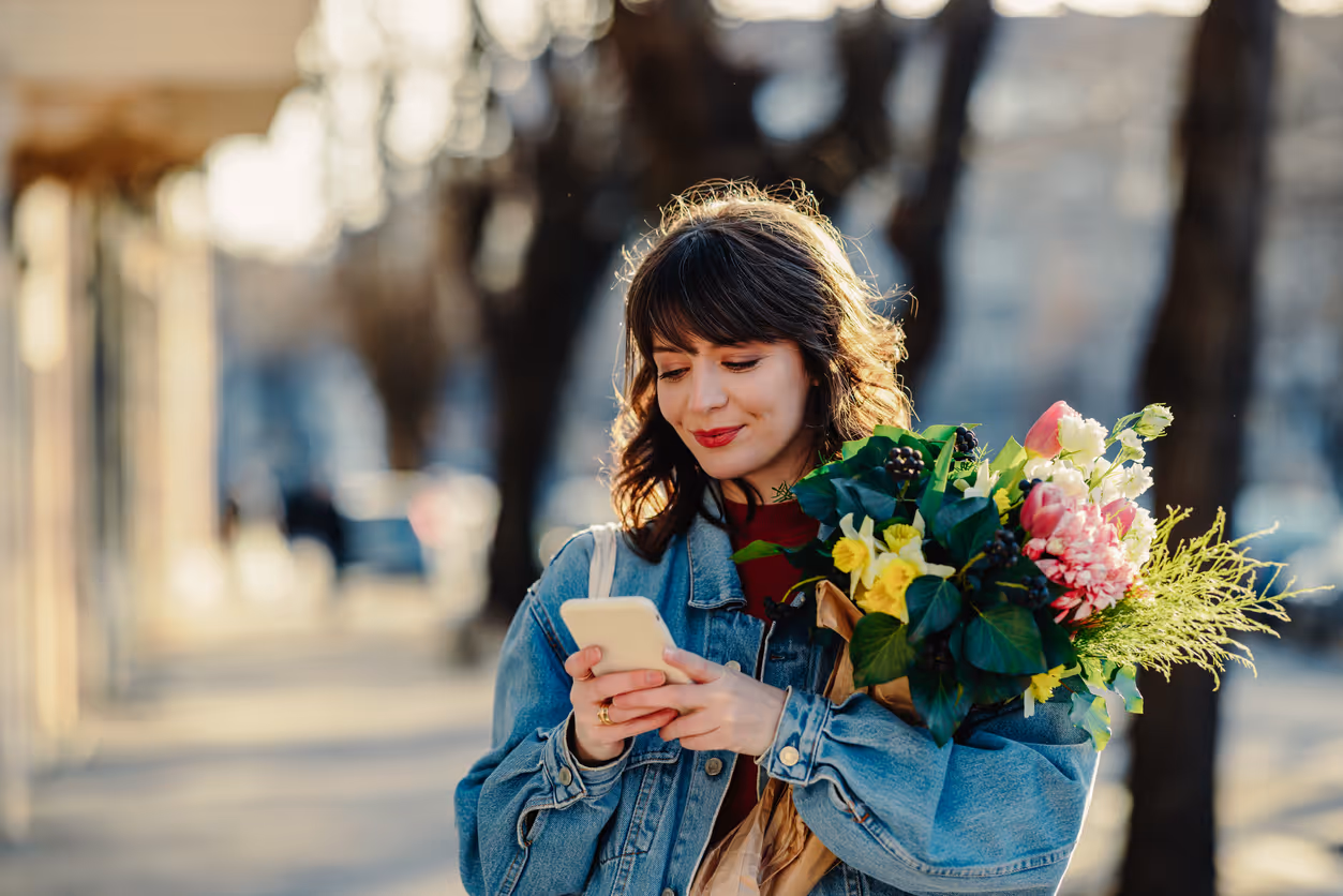 Glückliche Frau mit Blumenstrauß in der Hand am Smartphone.